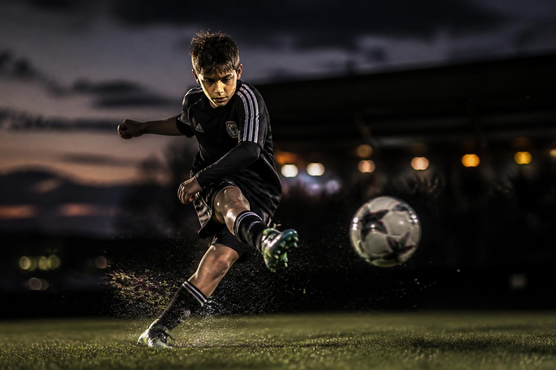 Junior footballer striking a ball under stadium floodlights